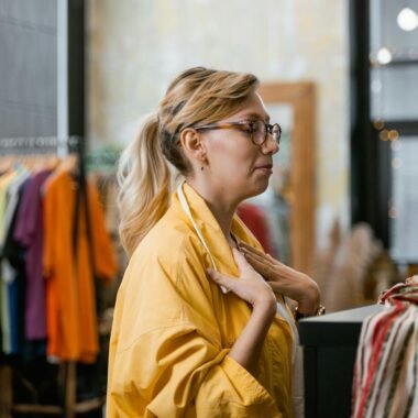 Woman in a yellow jacket shopping in a trendy boutique, exploring stylish clothing options.