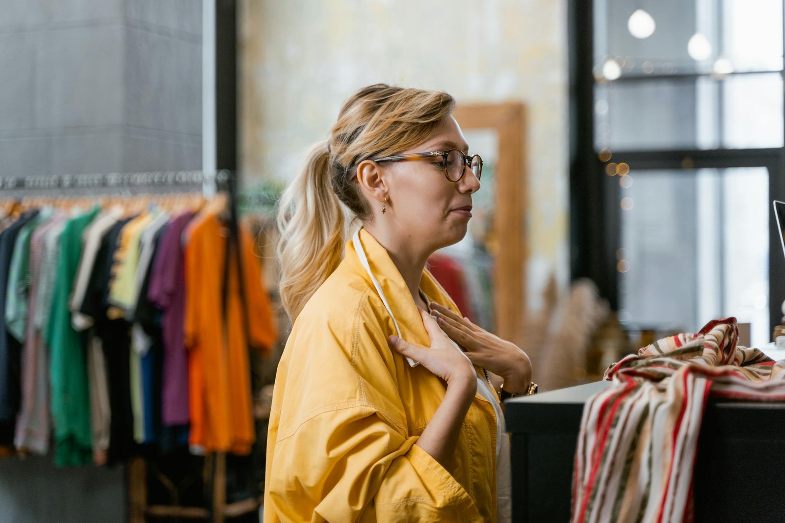 Woman in a yellow jacket shopping in a trendy boutique, exploring stylish clothing options.